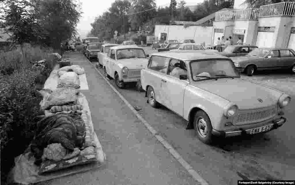 Беженцы из Восточной Германии спят рядом со своими автомобилями Trabant в Будапеште. После бархатной революции в Венгрии в 1989 году тысячи немцев из Восточной Германии, которые жили в условиях неусыпным контролем со стороны тайной полиции Штази, устремились на восток. Венгрия была одним из «братских социалистических государств», куда им разрешалось ездить