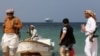 Вооруженные люди стоят на пляже, когда торговое судно Galaxy Leader, захваченное йеменскими хуситами в прошлом месяце, стоит на якоре у берегов Аль-Салифа.