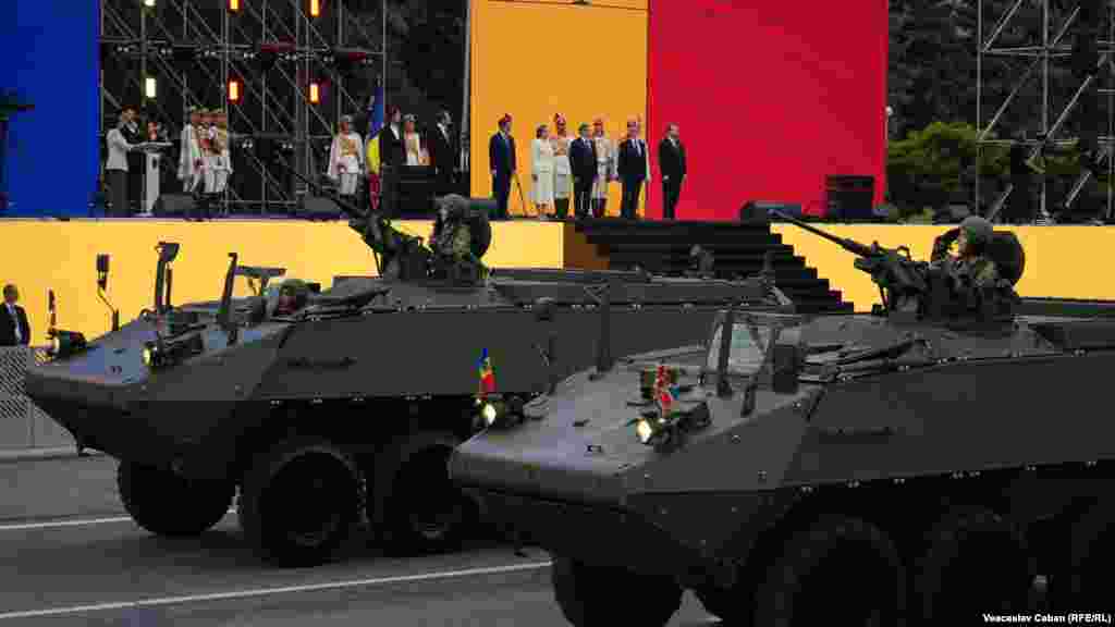 Transportoare blindate Piranha trec prin fața scenei din Piața Marii Adunări Naționale. Armata Națională a primit 19 transportoare Piranha 3H din partea Guvernului Germaniei, ultimul lot în noiembrie 2023, iar în iunie 2026 - alte cinci vehicule Piranha 5, tot ca donație germană.<br><br>
