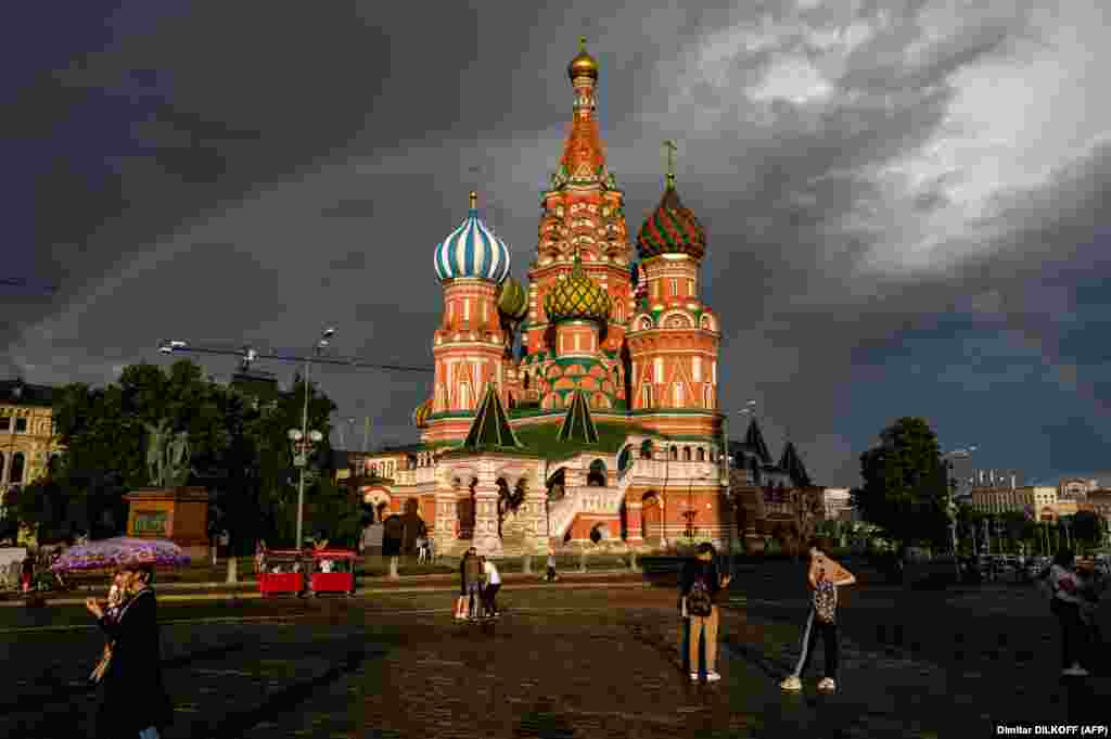 People walk in front of St. Basil&#39;s Cathedral lit by the sun with a rainbow in the background on Red Square in Moscow. (AFP/Dimitar Dilkoff)