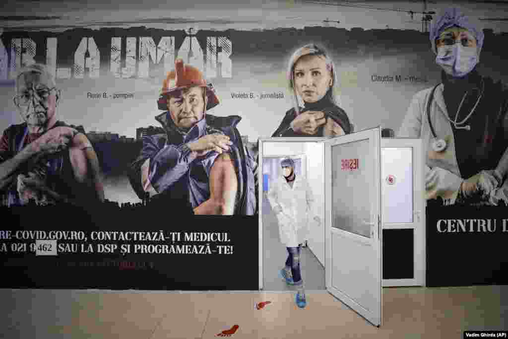 A medical worker walks under large posters advertising a COVID-19 inoculation campaign at a Bucharest vaccination center on March 23. (AP/Vadim Ghirda)