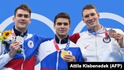 Yevgeny Rylov (center) of Russia won gold, Kliment Kolesnikov (left) of Russia won silver, and Ryan Murphy of the United States won bronze in the men's 100-meter backstroke swimming event in Tokyo.