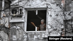 Жінка викидає уламки скла зі своєї квартири в будинку, ураженому російським дроном, 26 лютого 2026 року