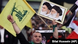 A Hezbollah supporter chants slogans, as he holds a picture of the late Iran revolutionary founder Ayatollah Khomeini, left, and Iran's Supreme Leader Ayatollah Ali Khamenei, right, during a Hezbollah-organized rally titled "in solidarity with oppressed Y