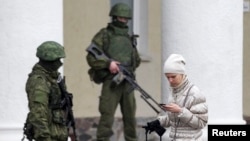 Ukraine -- A woman walks past armed men at the Simferopol airport in the Crimea region, February 28, 2014