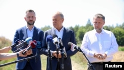 Premierul polonez Donald Tusk (centru) la conferința de presă organizată lângă locul unde a căzut racheta de croazieră.