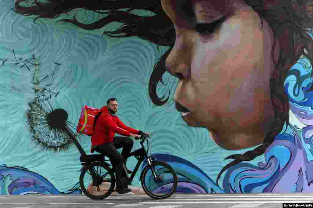 Мужчина проезжает на велосипеде мимо граффити в Белграде