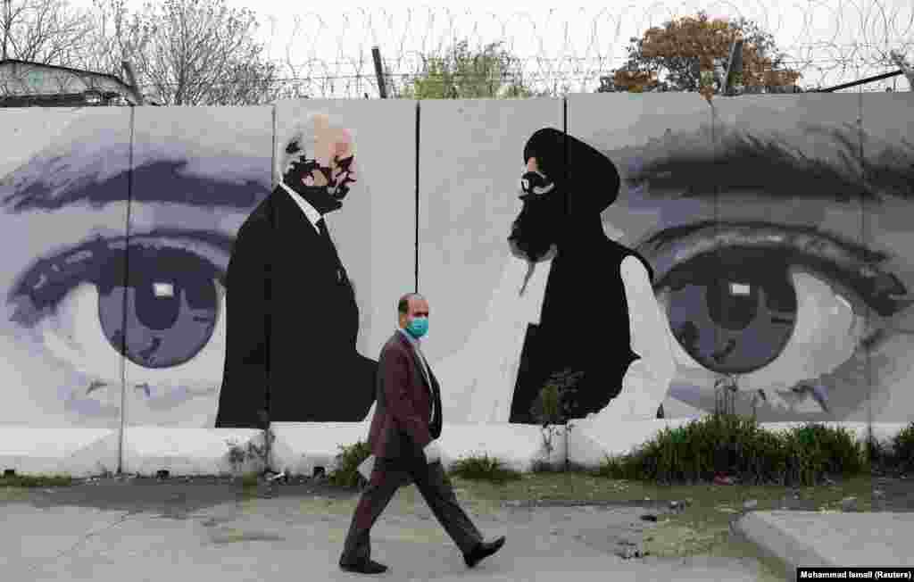 An Afghan man wearing a protective face mask walks past a wall painted with an image of Zalmay Khalilzad, U.S. envoy for peace in Afghanistan, and Mullah Abdul Ghani Baradar, the leader of the Taliban delegation, in Kabul. (Reuters/Mohammad Ismail)