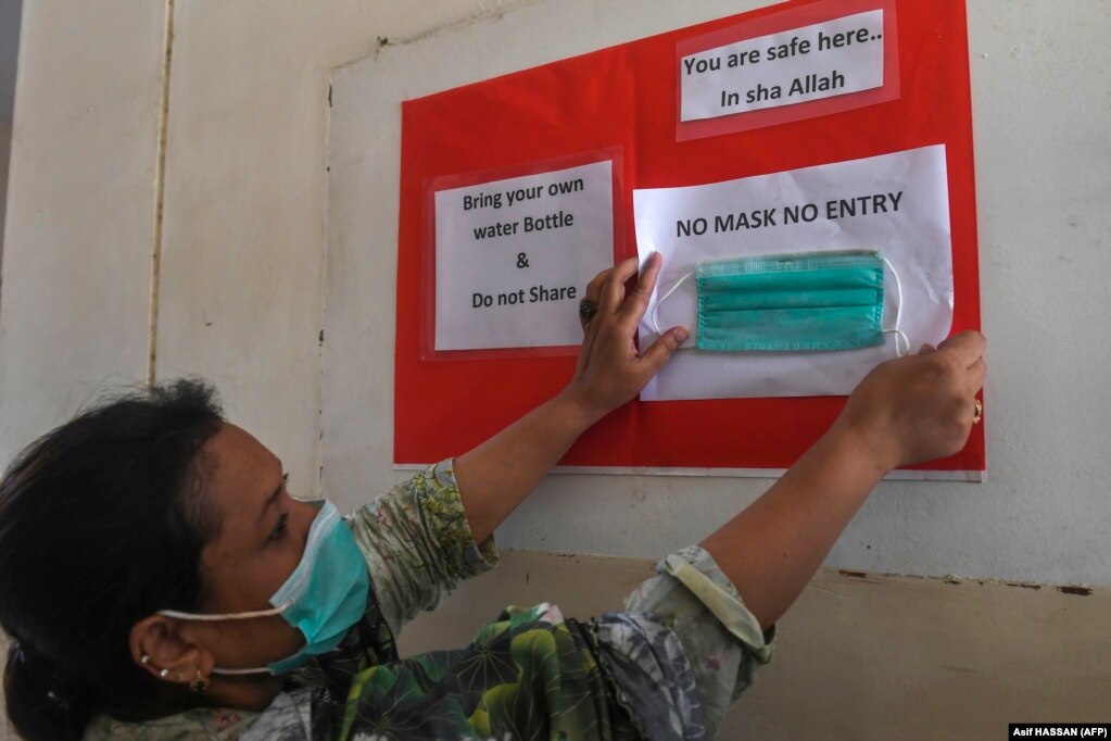 Вчитель вивішує табличку в урядовій школі у Карачі про те, що вхід без масок заборонений. Навчальний заклад відкрили після майже піврічного карантину