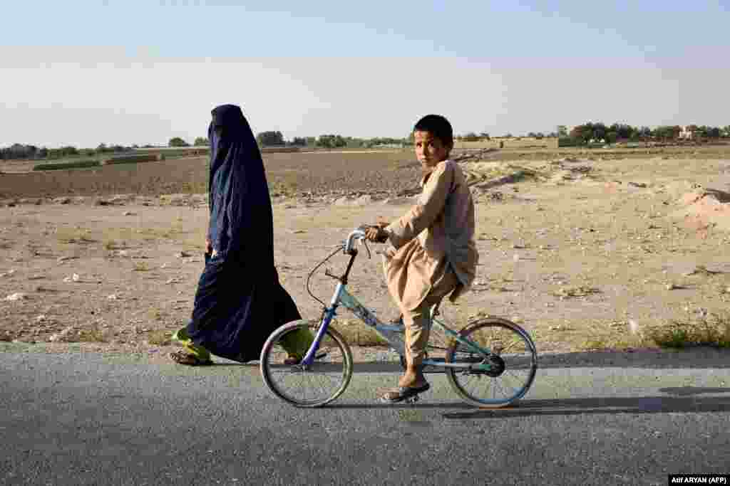 An Afghan boy rides a bicycle past a burqa-clad woman along a street on outskirts of Mazar-i-Sharif.