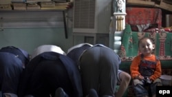 A child sits as older Uyghur Muslims pray at a mosque in Urumqi on July 9.