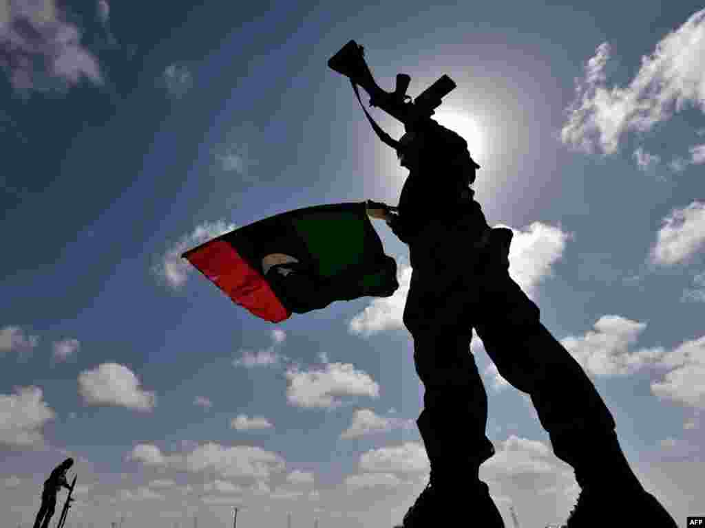 A Libyan anti-Qaddafi fighter waves the flag of the rebellion on a desert road some 30 kilometers before the eastern town of Brega on March 31, as rebels fought running street battles for the oil town, about 800 kilometers from Tripoli, with forces loyal to Libyan leader Muammar Qaddafi. Photo by AFP