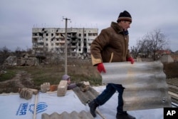 Un bărbat își ajută vecinul să repare un acoperiș după ce casele lor au fost distruse în timpul luptelor dintre forțele ruse și ucrainene în orașul Arhanhelske, recent recucerit, la începutul acestei luni.
