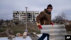 Мужчина помогает соседу чинить крышу, разрушенную во время боев между российскими и украинскими войсками. Посёлок Архангельское, 5 декабря 2022 года