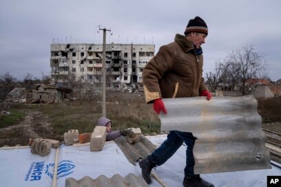 Një burrë ndihmon fqinjin e tij për të riparuar një çati pasi shtëpitë e tyre u shkatërruan gjatë luftimeve midis forcave ruse dhe ukrainase në qytetin e rimarrë së fundmi të Arhanhelske në fillim të këtij muaji.