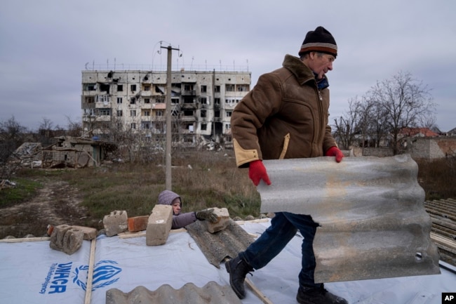 A man helps his neighbor to repair a roof after their houses were destroyed during fighting between Russian and Ukrainian forces in the recently retaken town of Arhanhelske earlier this month.