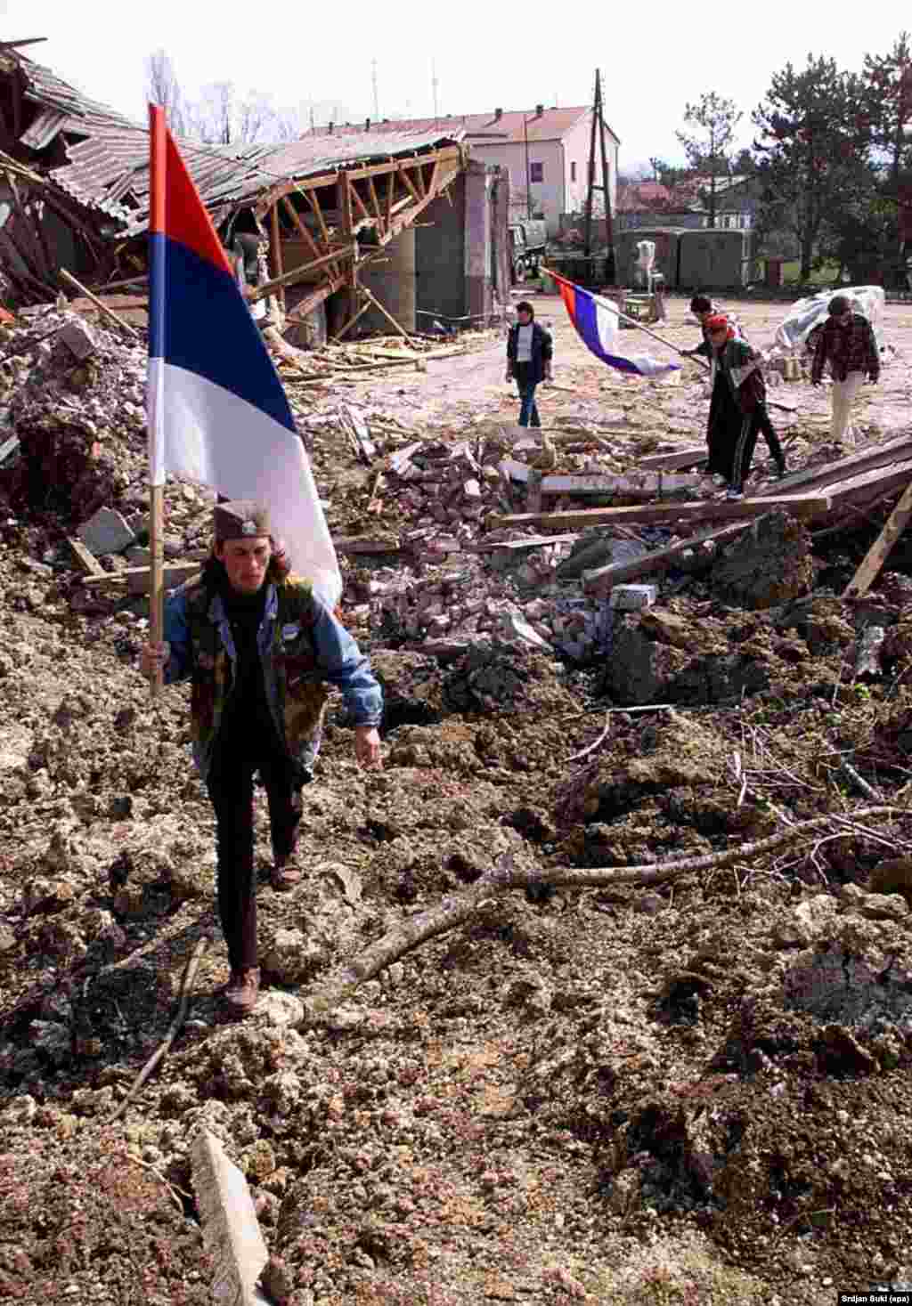 Men carrying Serbian flags and wearing traditional caps walk through the rubble left after NATO jets bombed a Yugoslav Army base in Kragujevac in 1999.