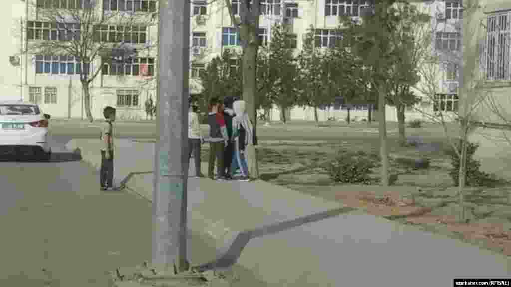 Köçäniň gyrasynda gürleşp duran çagalar. Olaryň bir ýüz maskasyny geýipdir. Aşgabat, fewral, 2021.