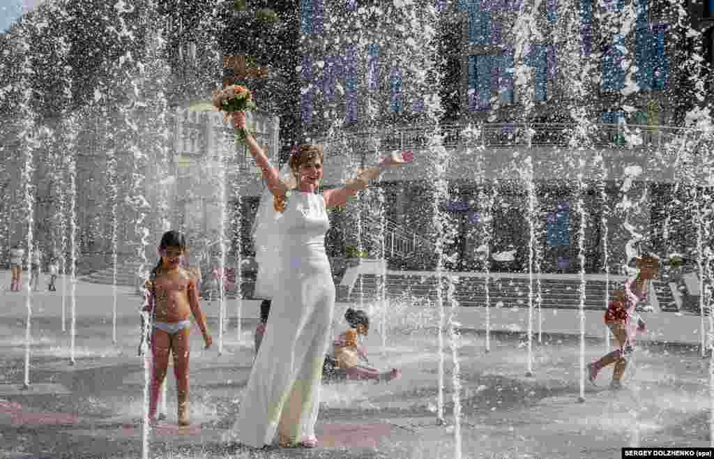 A bride walks in a fountain on a hot summer day in Kyiv, where temperatures reached over 36 degrees Celsius. (epa/Sergey Dolzehnko)