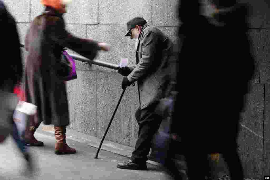 A woman drops a few coins into the cup of an old man asking for alms as people rush by in an underground passage in the center of St. Petersburg, Russia. (epa/Anatoly Maltsev)