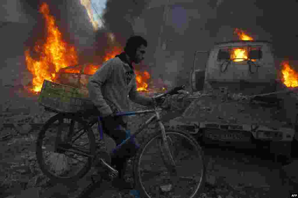 Человек с велосипедом пробрается мимо горящих машин в сирийском городе Хамурия, по которому, как сообщается, был нанесен авиаудар.&nbsp;