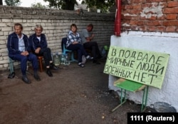 Residents sit near a shelter where they were hiding during recent fighting between Ukrainian and Russian forces in Russia's Kursk region. The poster reads: "Civilians in the basement, no soldiers."