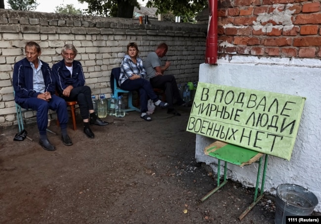 Residents sit near a shelter where they were hiding during recent fighting between Ukrainian and Russian forces in Russia's Kursk region. The poster reads: "Civilians in the basement, no soldiers."