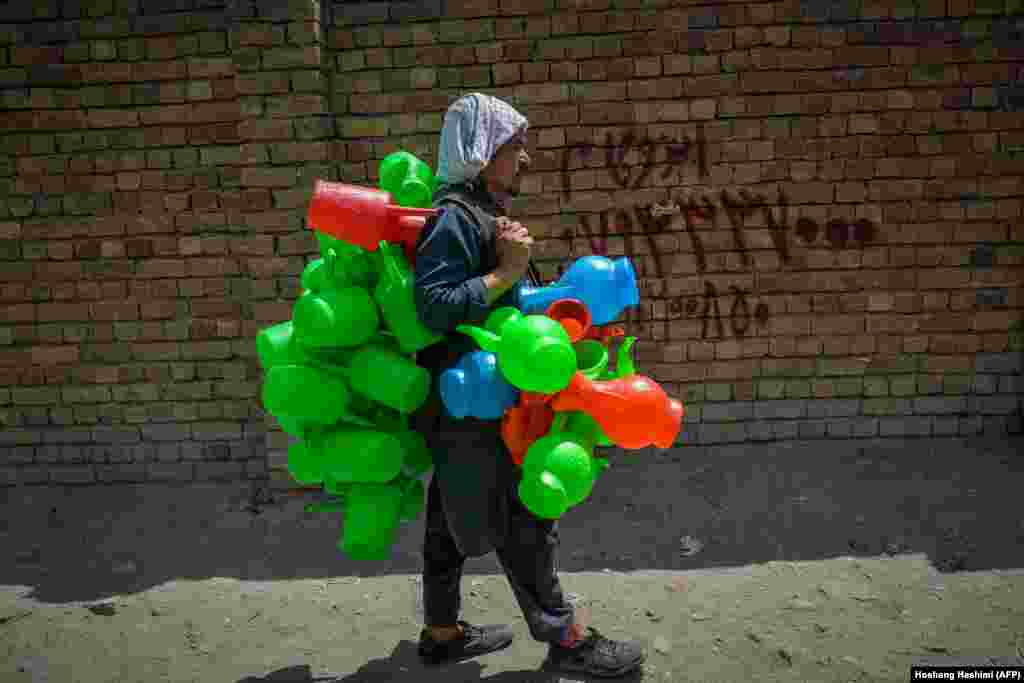 Торговец пластиковыми контейнерами идет по улице в районе рынка в Кабуле, Афганистан