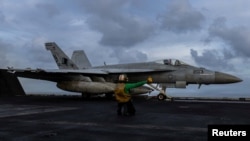 Un soldat al Marinei SUA se pregătește să lanseze un avion F/A-18E Super Hornet de pe puntea portavionului USS Abraham Lincoln.