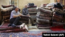 In this Aug. 10, 2015 file photo, Iranian merchants wait for customers at a carpet shop in Tehran's old, main bazaar, Iran.