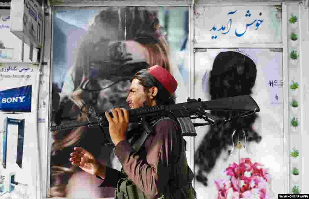 A Taliban fighter with an American-made rifle walks past a beauty salon with images of women defaced using spray paint in Shar-e-Naw.
