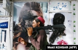 Сыртқы жарнамасындағы әйел бейнесіне қара бояу жағылып, жұмысы тоқтап тұрған сұлулық салоны қасынан өтіп бара жатқан "Талибан" қарулы жасағы. Кабул, Ауғанстан, 18 тамыз 2021 жыл.