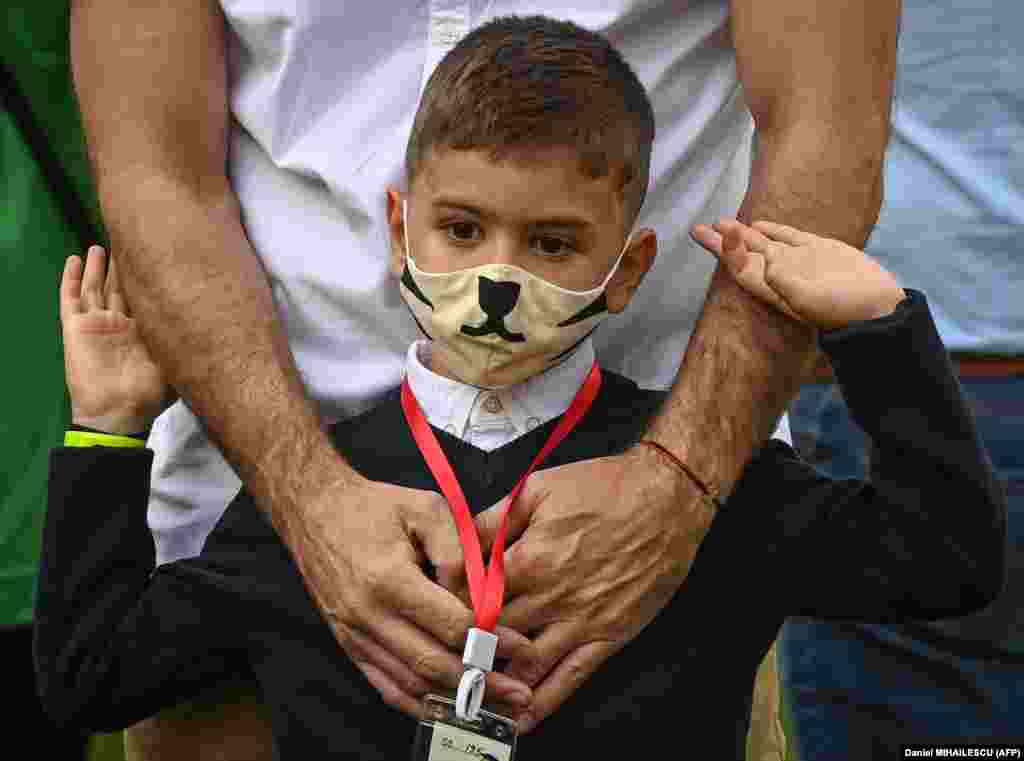 Дете с предпазна маска чака заедно с баща си началото на учебната година пред училище в Букурещ.