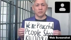 Гражданский активист Асхат Жексебаев на онлайн-суде держит плакат, на котором на английском языке написано: «Мы мирные люди. Прекратите нас убивать!» Алматы, 28 сентября 2021 года