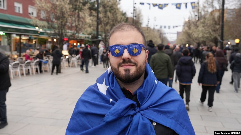 Një burrë i mbështjellë me flamurin e Kosovës shihet në sheshin e Prishtinës, disa orë para ndeshjes vendimtare mes Kosovës dhe Turqisë për një vend në Kupën e Botës 2026, të martën në Stadiumin "Fadil Vokrri".
