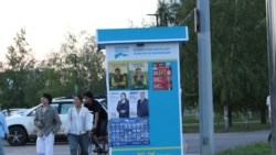 Сайлау алдындағы үгіт-насихат қағаздары ілінген стендтің жанынан өтіп бара жатқан жастар. Астана 2026 жылғы шілде.