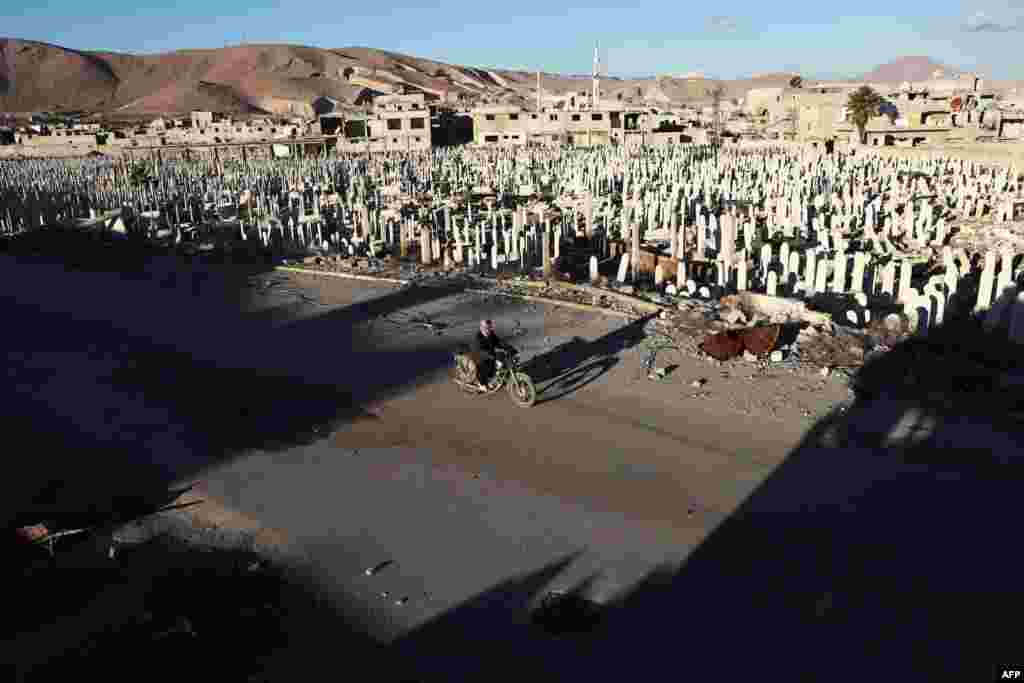 A Syrian man rides a motorbike past a cemetery in the rebel-held town of Douma, on the eastern outskirts of Damascus, Syria. (AFP/Abd Doumany)