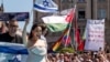 Reprezentanta Israelului Yuval Raphael pășește pe covorul turcoaz la ceremonia de deschidere a Eurovision 2025, pe fundalul protestatarilor care țin drapele palesteniene și pancarte prin care cer eliminarea Israelului din concurs. Basel, Elveția, 11 mai 2025.