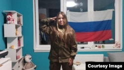Alisa salutes with a Russian flag in the background.