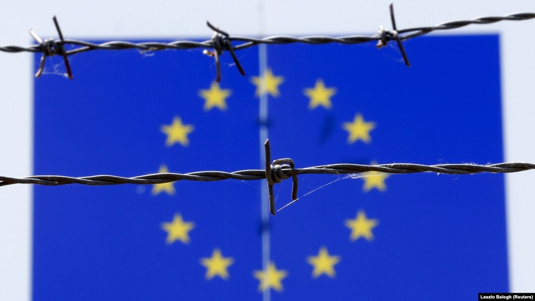 Sârmă ghimpată văzută în fața unui steag al Uniunii Europene la un centru de primire a imigranților din Bicske, Ungaria, 25 iunie 2015. La aproape zece ani de atunci și după trei ani de negocieri, UE a ajuns la un acord privind migranții.