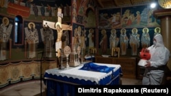 A worker in a protective suit disinfects the church of the Kastritsis Monastery Работник с предпазно облекло извършва дезинфекция на църква в гръцкия манастир в Кастрица