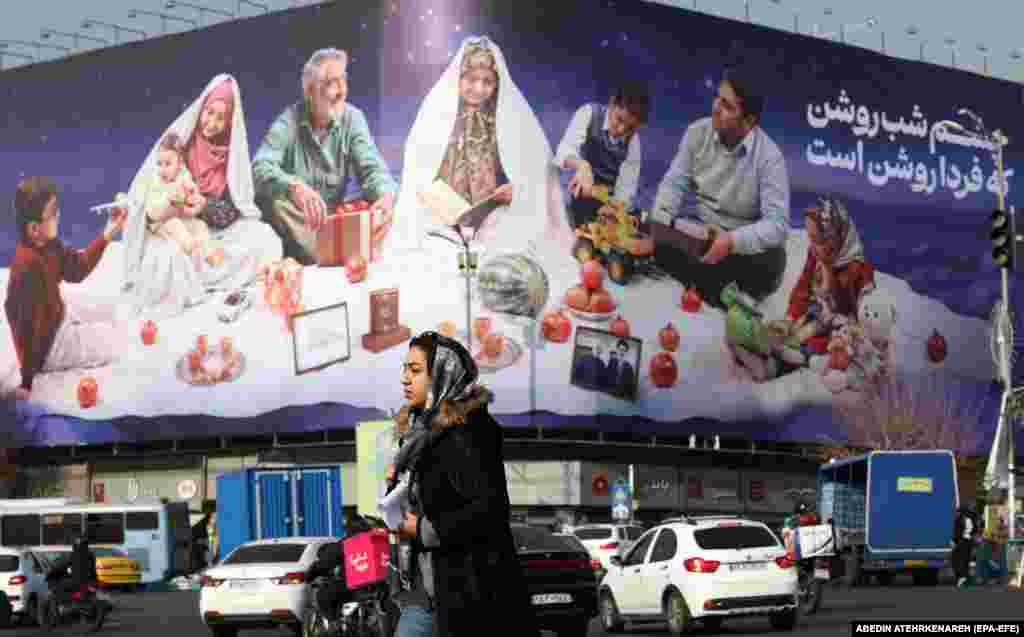 Një grua iraniane duke ecur para një pllakati që shfaq një familje tradicionale iraniane, në sheshin Enghelab, në Teheran.