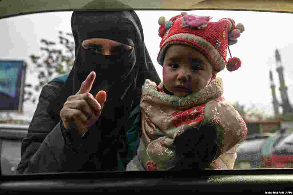 A woman carries a child as she begs for money from commuters in a car in Kabul.