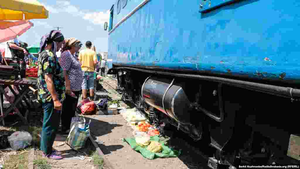 Торговці дивляться на свій товар, над яким проїжджає тепловоз. Зазвичай, вони його не прибирають з колій