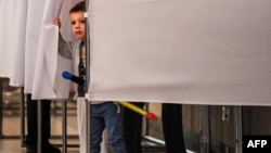 A young boy peeps out from behind the curtains of a voting booth at a polling station during the municipal elections in Moscow on September 10. 