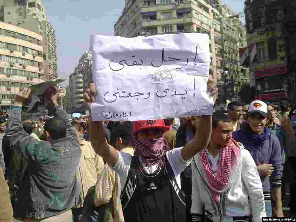 A young protester holds a banner reading "Go away then, my arm is hurting."