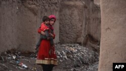 An Afghan girl holds her brother as she walks through a refugee camp in Herat in January.