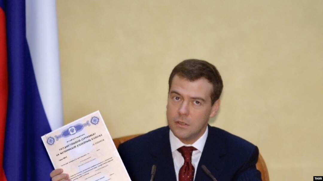 Рождение патриотов Россия стимулирует разными способами. Будущий президент страны держит в руках сертификат «материнского капитала» (январь 2007 года)