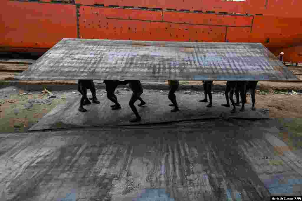 Bangladeshi laborers carry a heavy steel plate in a dockyard beside the Buriganga River in Dhaka. (AFP/Munir Uz Zaman)