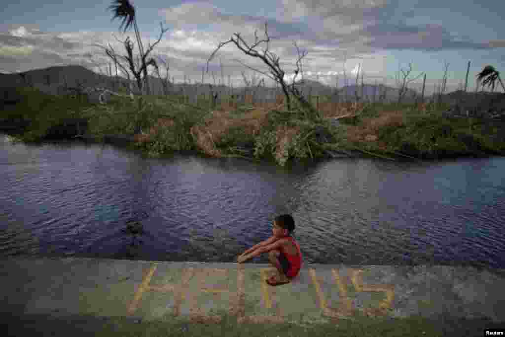 A boy sits on a message asking for help written in an area damaged by Typhoon Haiyan in Palo, Phillipines. (Reuters/John Javellana)